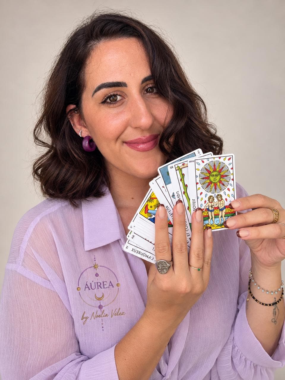 Noelia Vélez sonriendo con un abanico de cartas del Tarot de Marsella en la mano